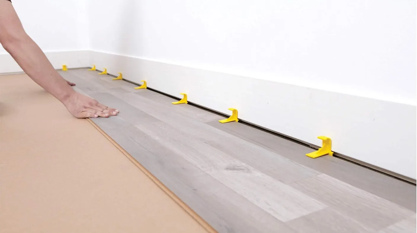 Calzadores de plástico colocados entre el piso flotante y la pared para mantener una junta de expansión uniforme durante la instalación.