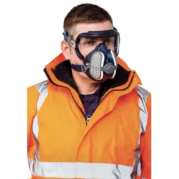 Técnico con equipo de protección completo —respirador de media cara y gafas selladas— durante una tarea con generación de polvo.