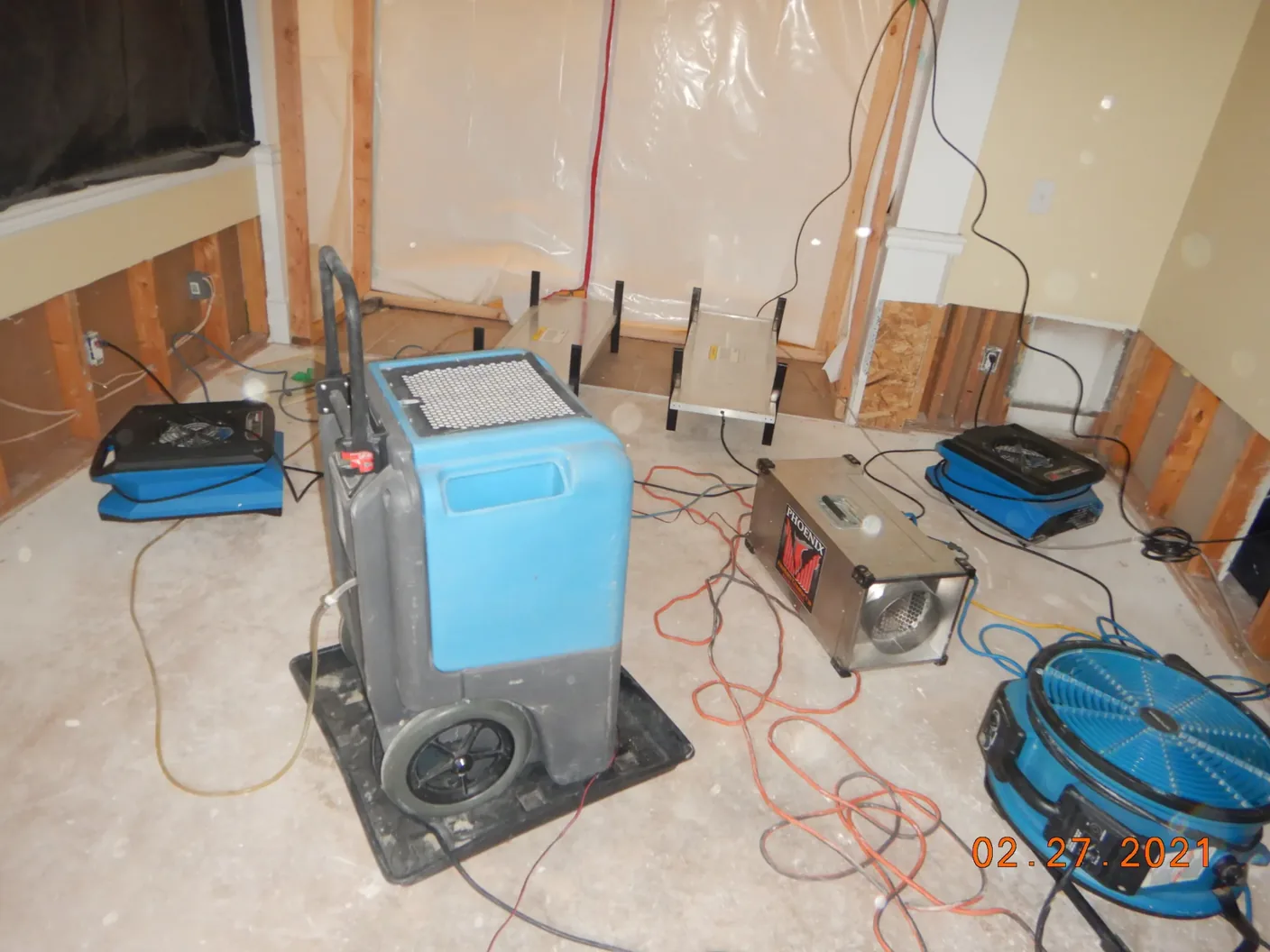 Equipo profesional de secado —ventiladores de aire y deshumidificadores— trabajando en un ambiente afectado por el agua durante una restauración.